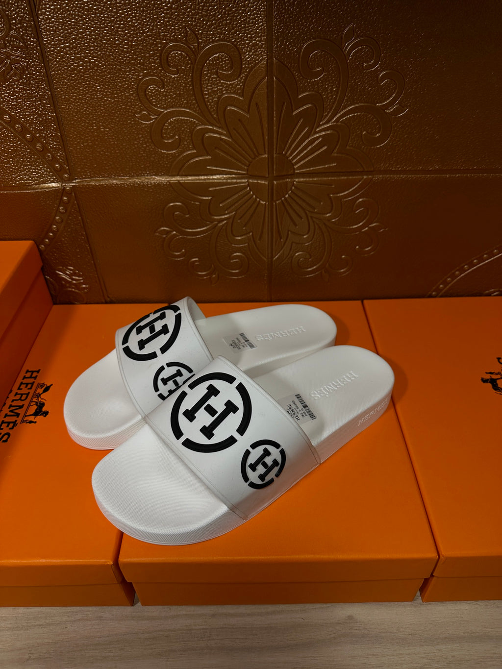 White slide sandals with black logo strap, angled front view