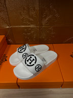 White slide sandals with black logo strap, angled front view