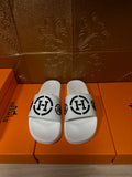 White slide sandals with black interlocking logo strap