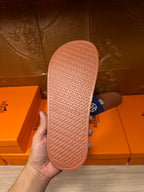 Blue slide sandal with tan patterned outsole, sole view held by hand