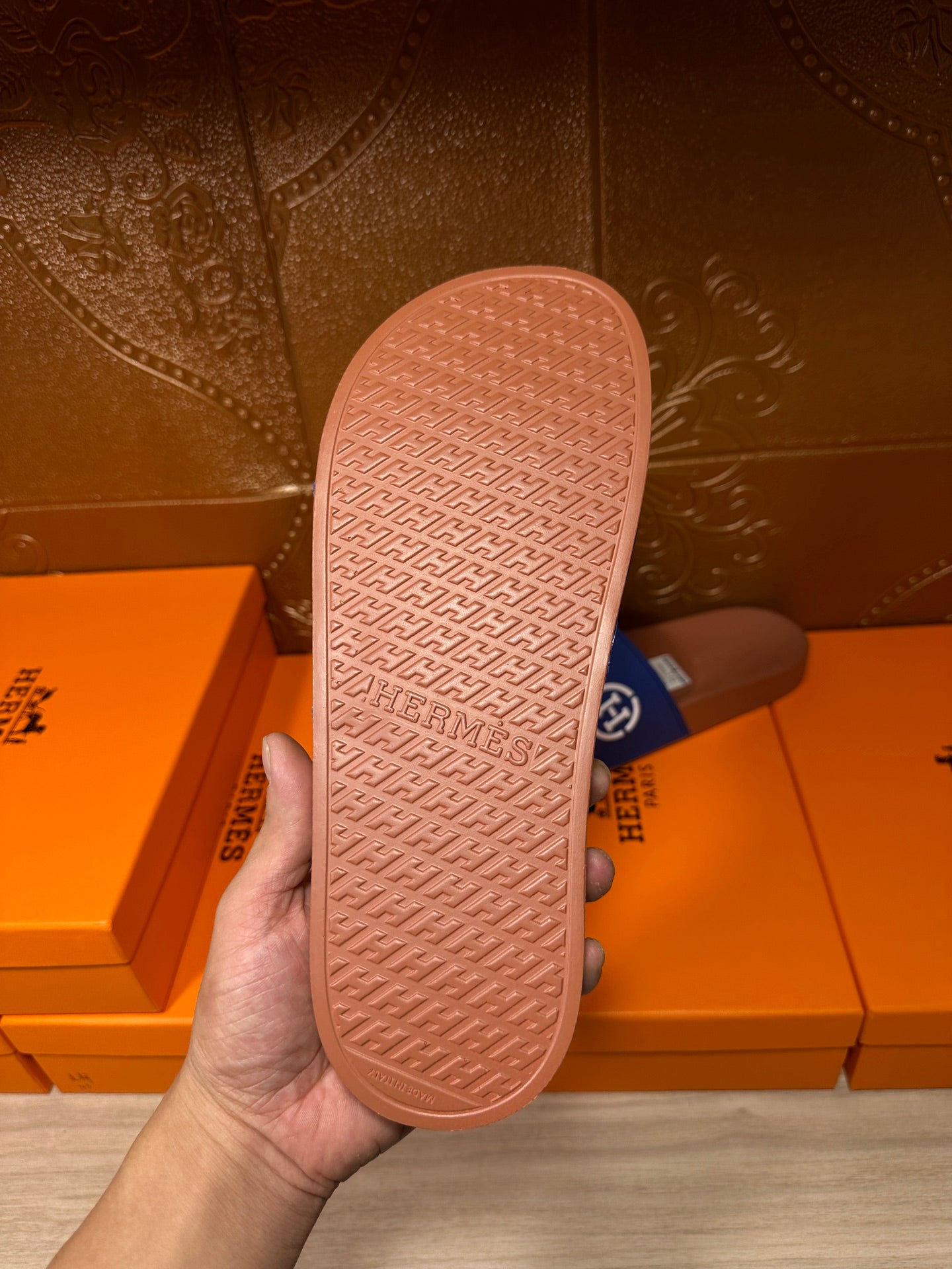 Blue slide sandal with tan patterned outsole, sole view held by hand