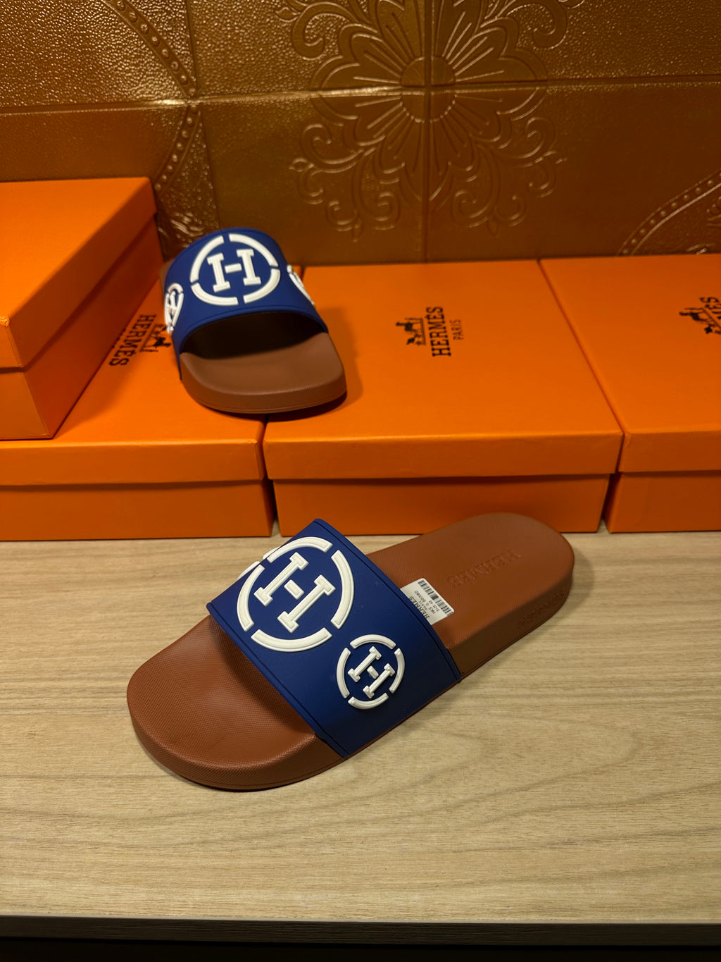 Blue logo slide sandals with brown footbeds, one upright on shoeboxes