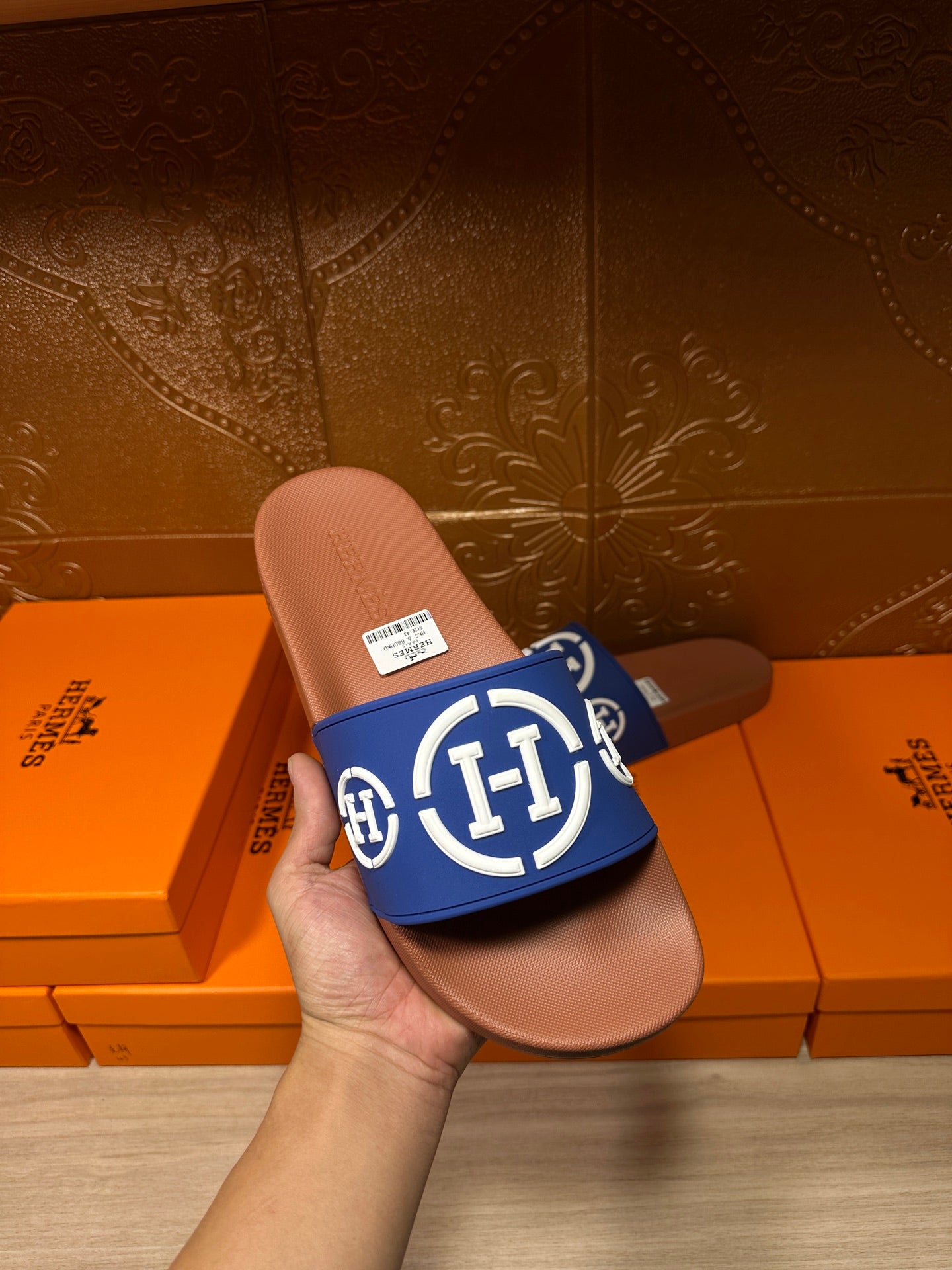Blue slide sandal with white logo emblem on tan footbed, held in hand