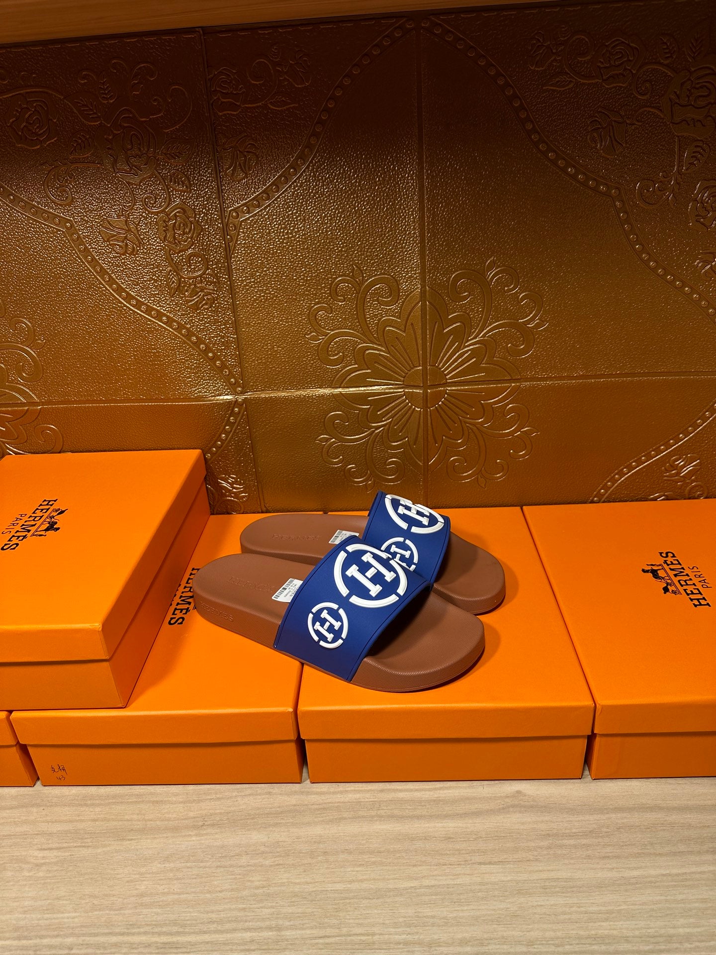 Blue slide sandals with white emblem logo and brown footbed, single shoe on shoebox