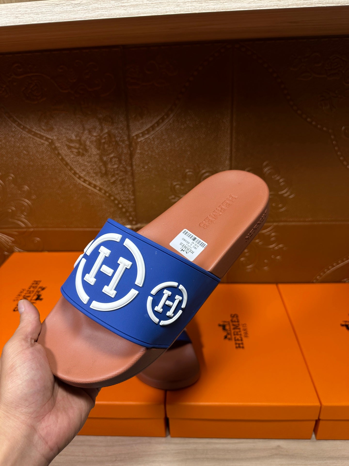 Blue slide sandal with white emblem logo on tan footbed, held in hand