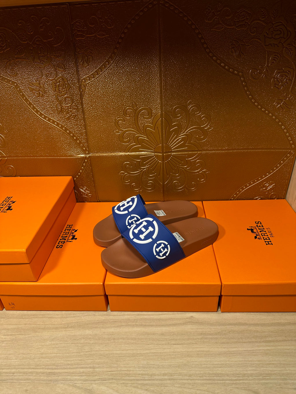 Blue logo slide sandals with brown footbeds, two shoes on orange shoeboxes