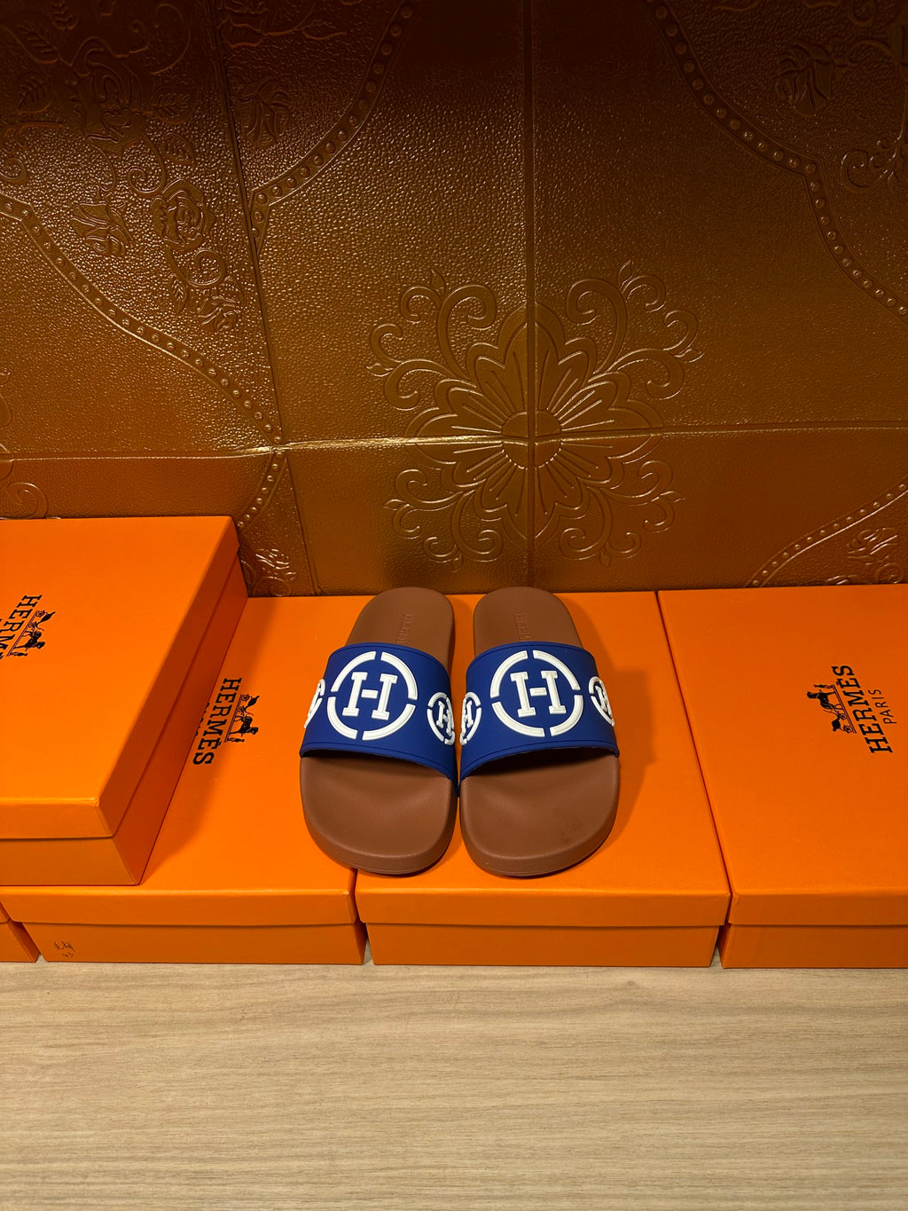 Blue slide sandals with white logo on brown footbeds, pair on shoeboxes