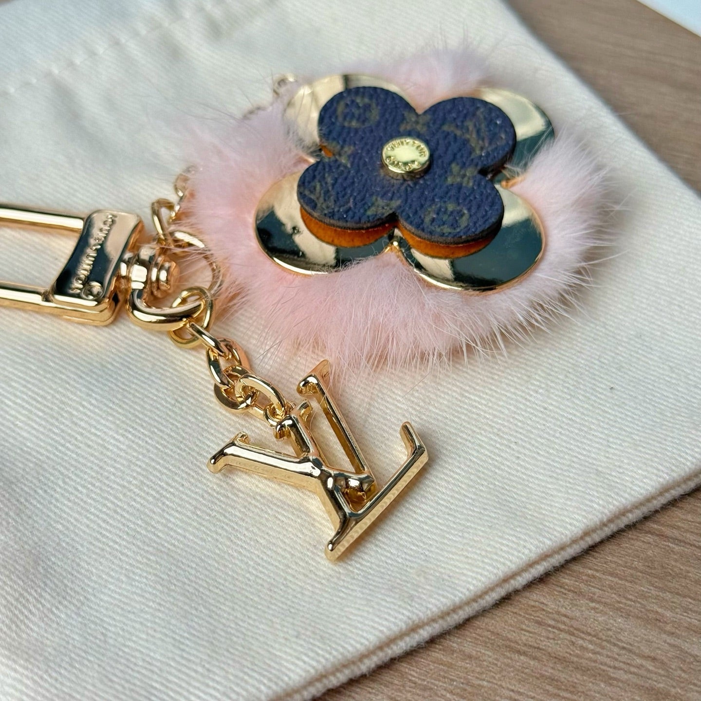 Louis Vuitton keychain close-up with blue flower charm, gold emblem, and pink fur