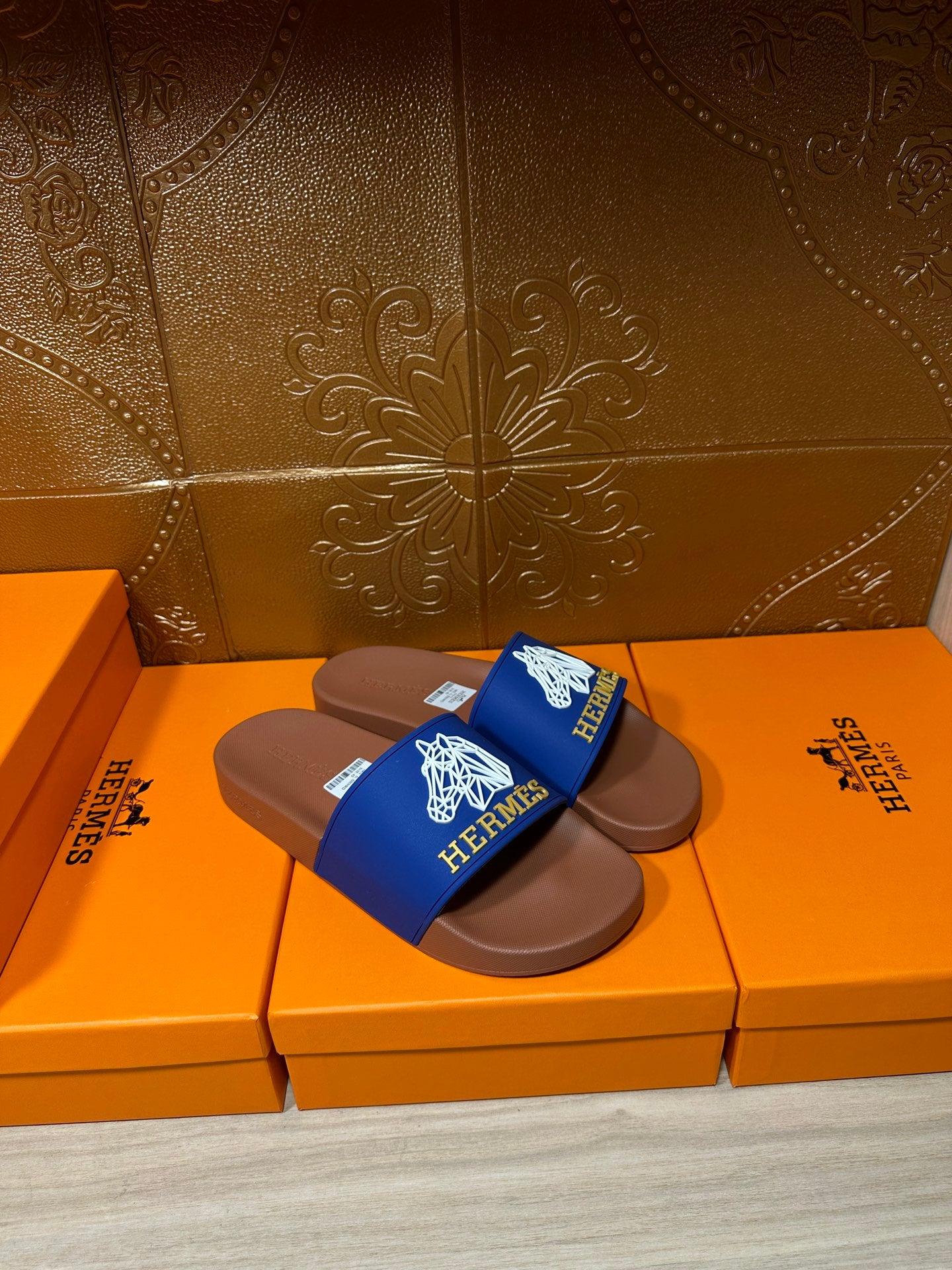 Hermes slide sandals with blue logo straps and brown soles on orange boxes
