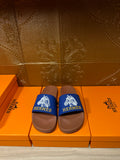 Hermes slide sandals with blue logo straps and brown footbeds on a box