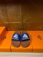 Hermes slide sandals with blue logo straps and brown footbeds on a box