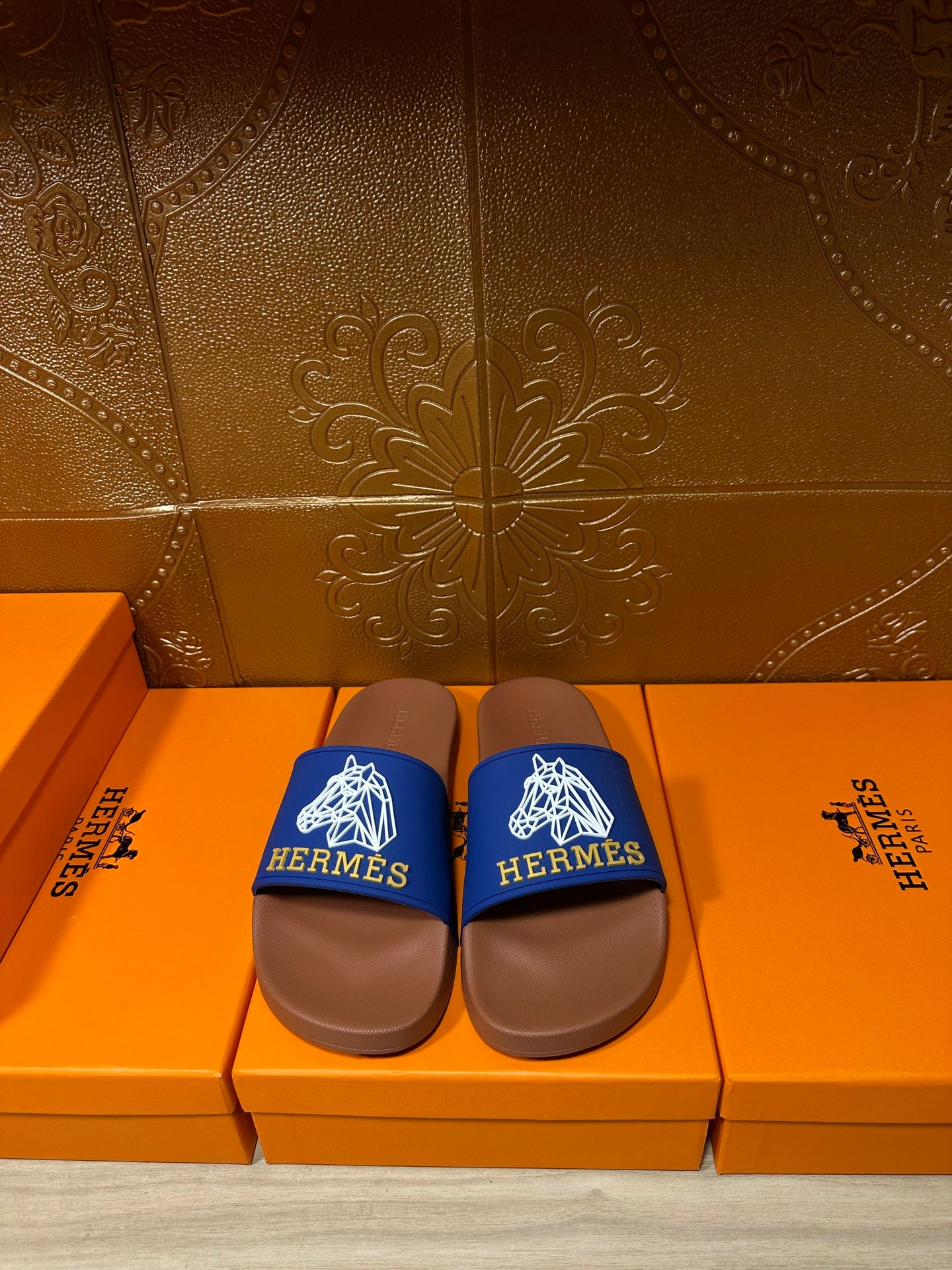 Hermes slide sandals with blue logo straps and brown footbeds on a box