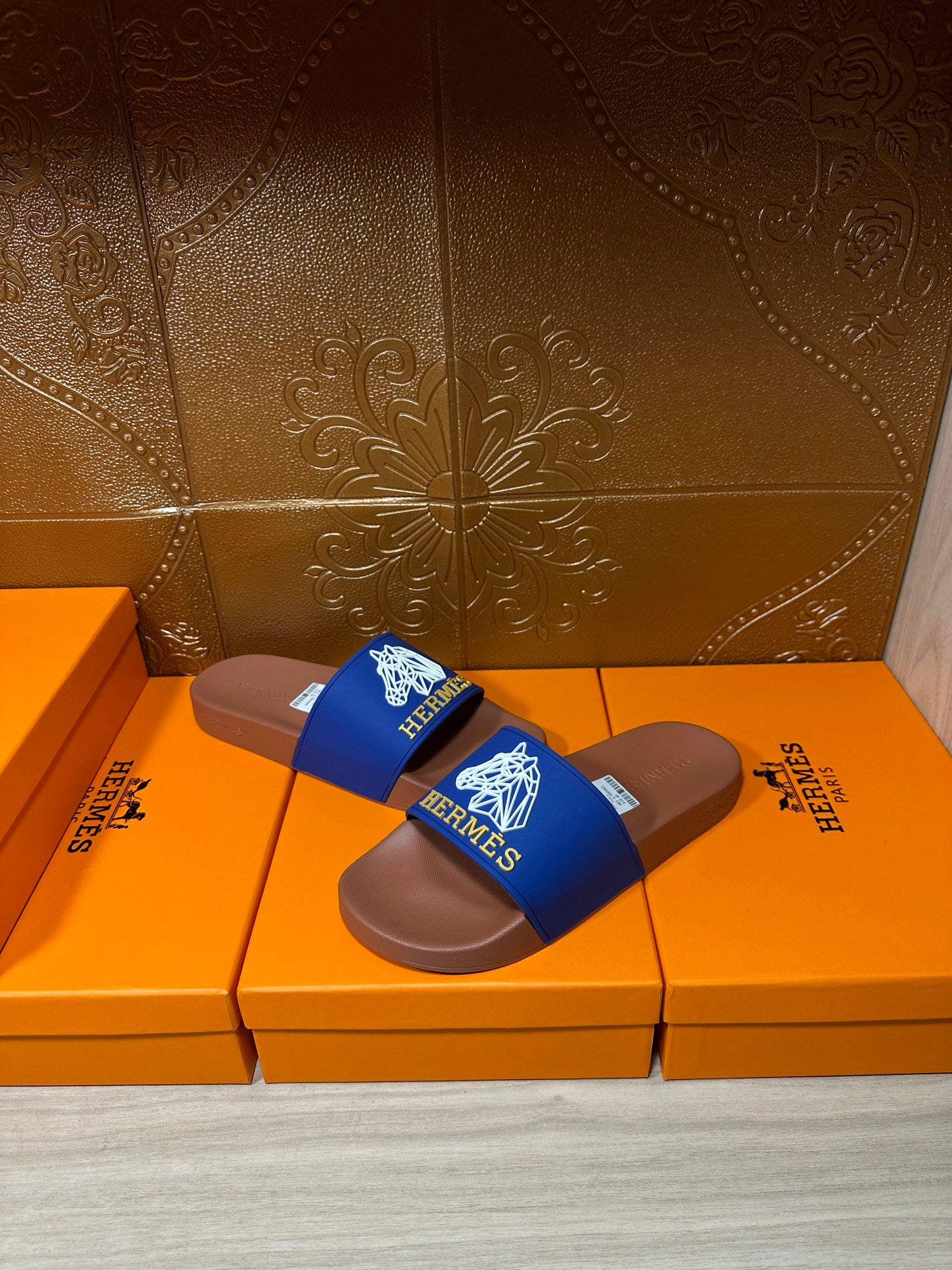 Hermes slide sandals with blue logo strap and brown footbed on orange boxes
