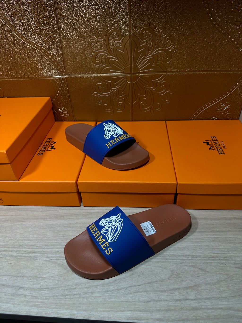 Hermes slide sandals with blue logo strap and brown footbed, laid on boxes