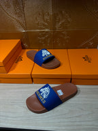 Hermes slide sandals with blue logo strap and brown footbed, laid on boxes
