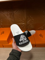 Hermes slide sandals held in hand, white footbed and black strap with Hermes branding