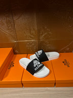 Hermes slide sandals, front view with white sole and black strap featuring Hermes logo print