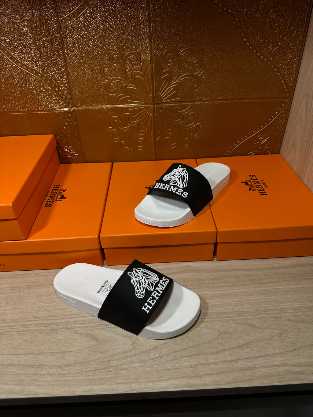 Hermes slide sandals with white footbed and black strap, placed atop orange gift boxes