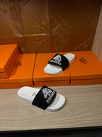 Hermes slide sandals with white footbed and black strap, placed atop orange gift boxes