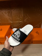 Hermes slide sandal in hand, white sole and black strap with white Hermes logo detail