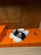 Hermes slide sandals, angled view with white sole and black wide strap with Hermes emblem
