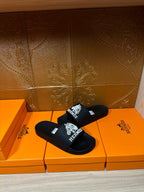 Hermes black slide sandals with white logo graphic on the wide strap