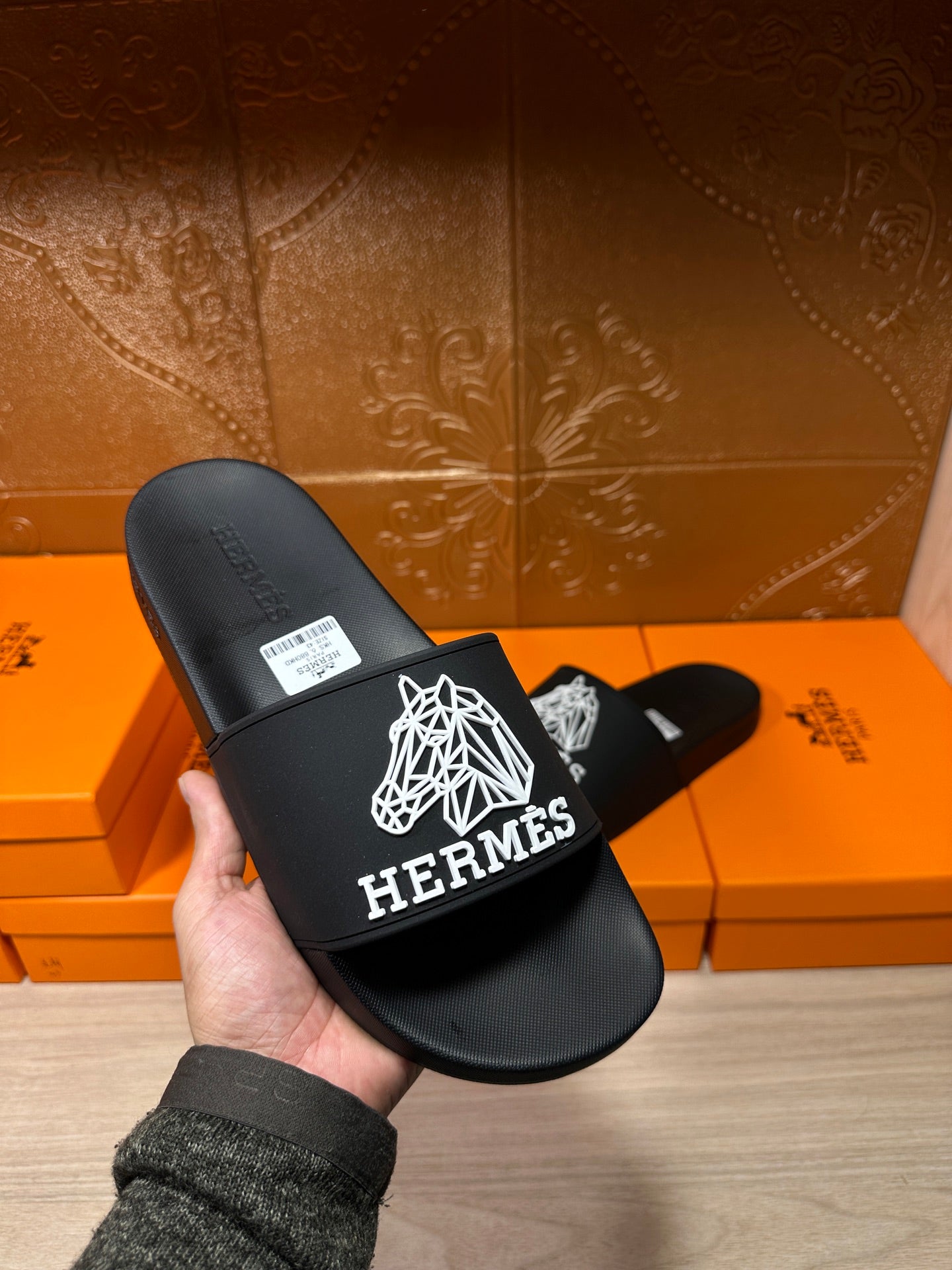 Hermes black slide sandals held in hand, white logo graphic on wide strap