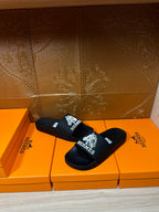 Hermes black slide sandals with white Hermes logo text and graphic on strap