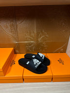 Hermes black slide sandals with white Hermes logo graphic on the strap