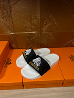 Hermes slide sandals with black strap and white geometric emblem over white footbed