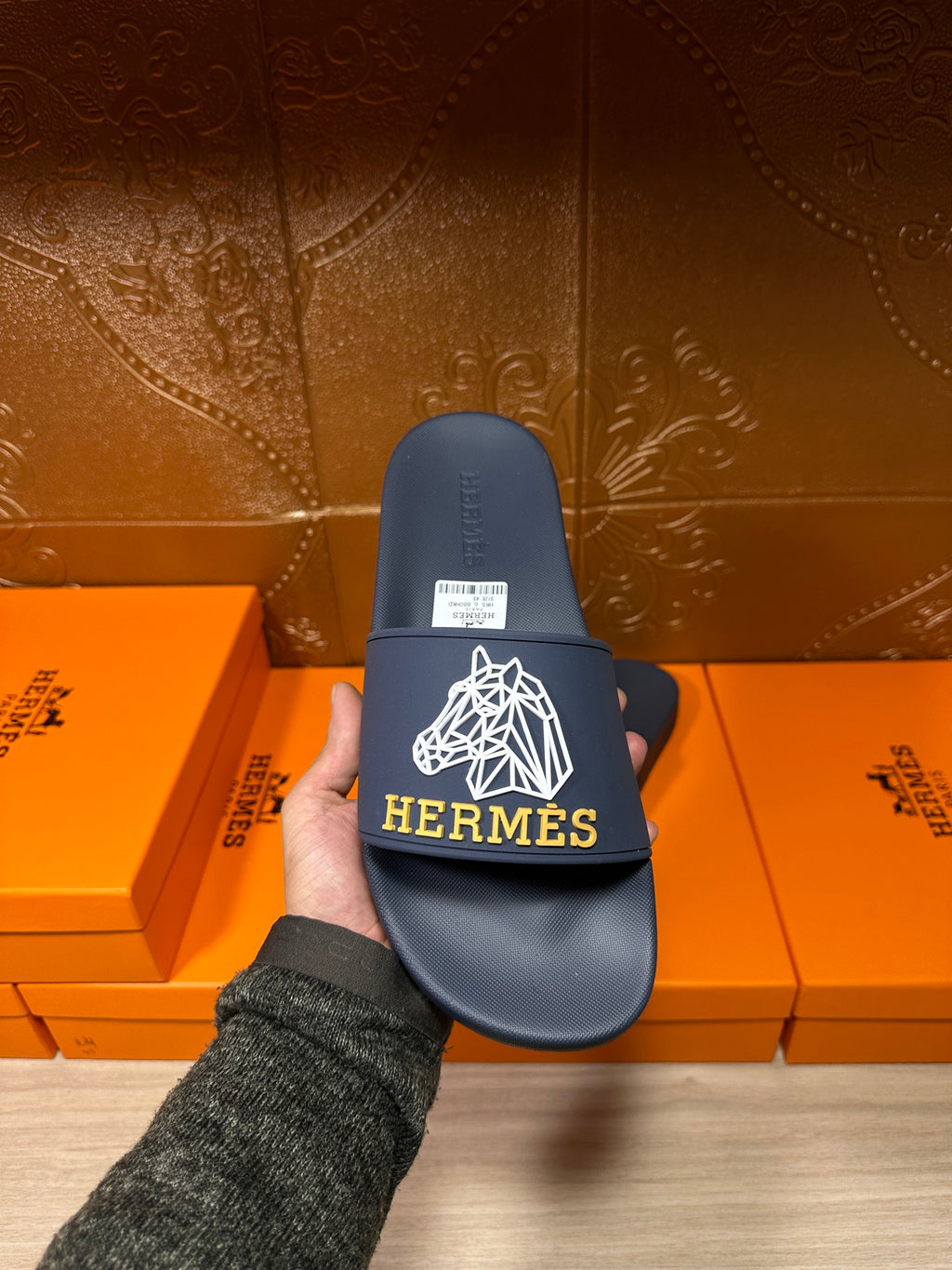 Navy slide sandal with white HERMES logo on front strap, held in hand