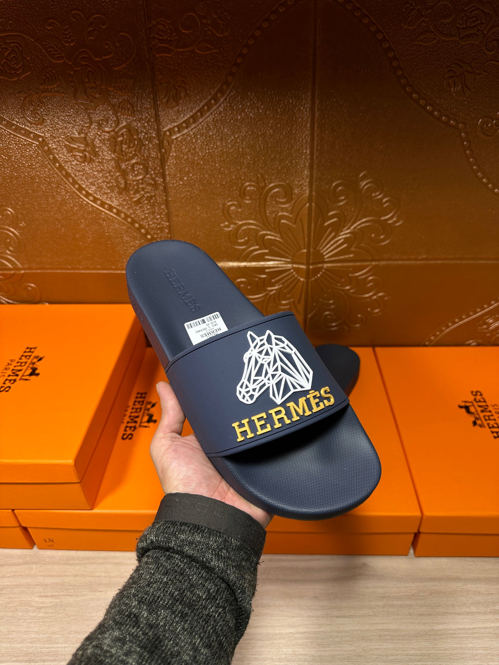 Navy slide sandal with white HERMES logo on wide strap, held in hand