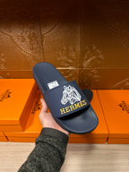 Navy slide sandal with white HERMES logo on wide strap, held in hand