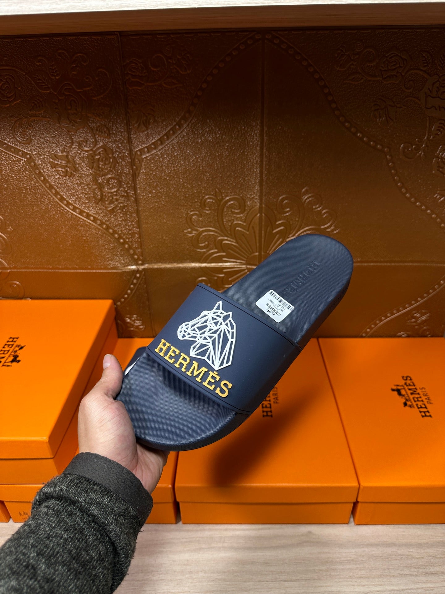 Navy slide sandal with white HERMES logo on wide strap, held in hand