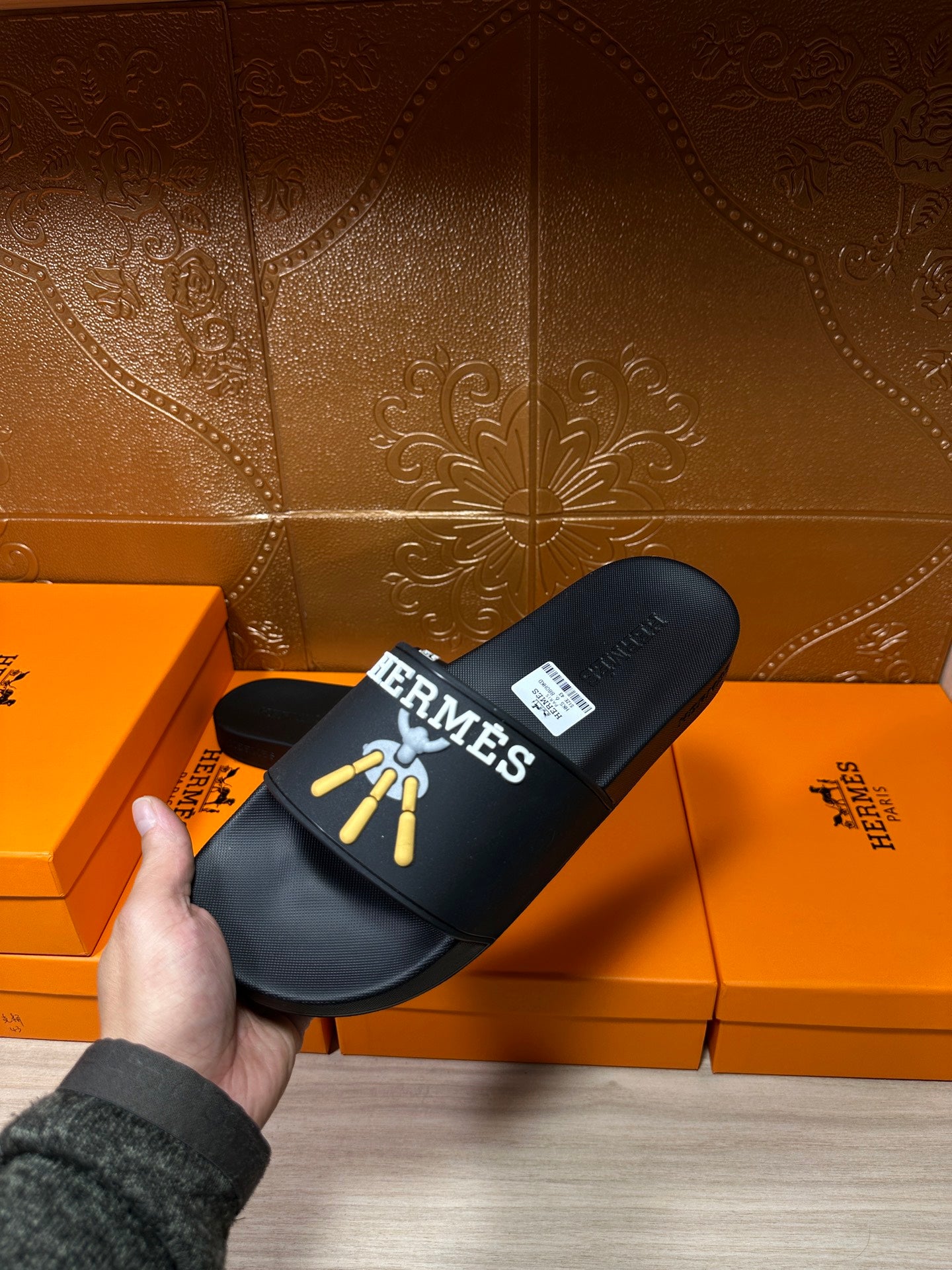 Hermes black slide sandal held up, gold logo graphic on upper