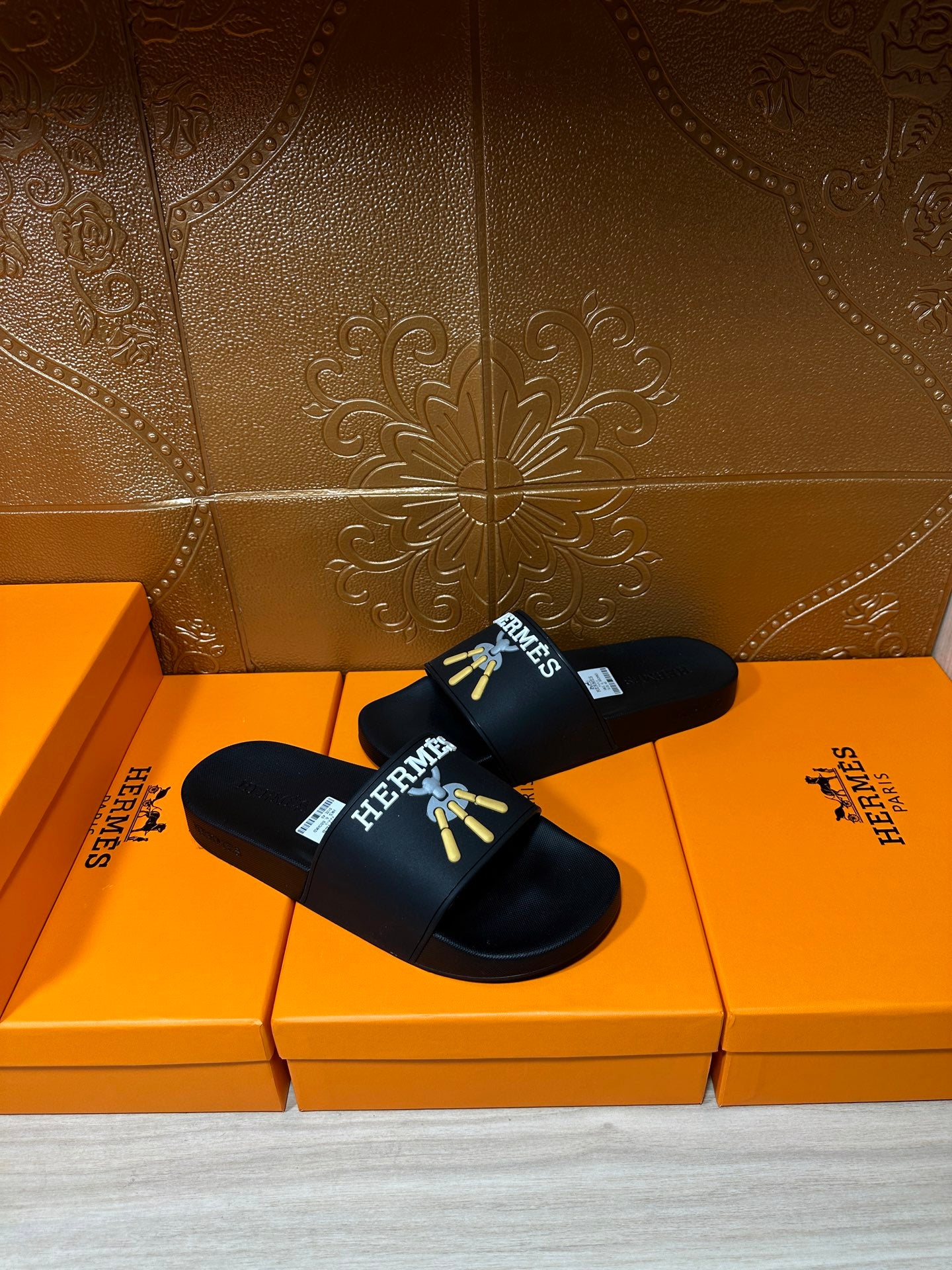 Hermes black slide sandals with gold logo graphic across the upper