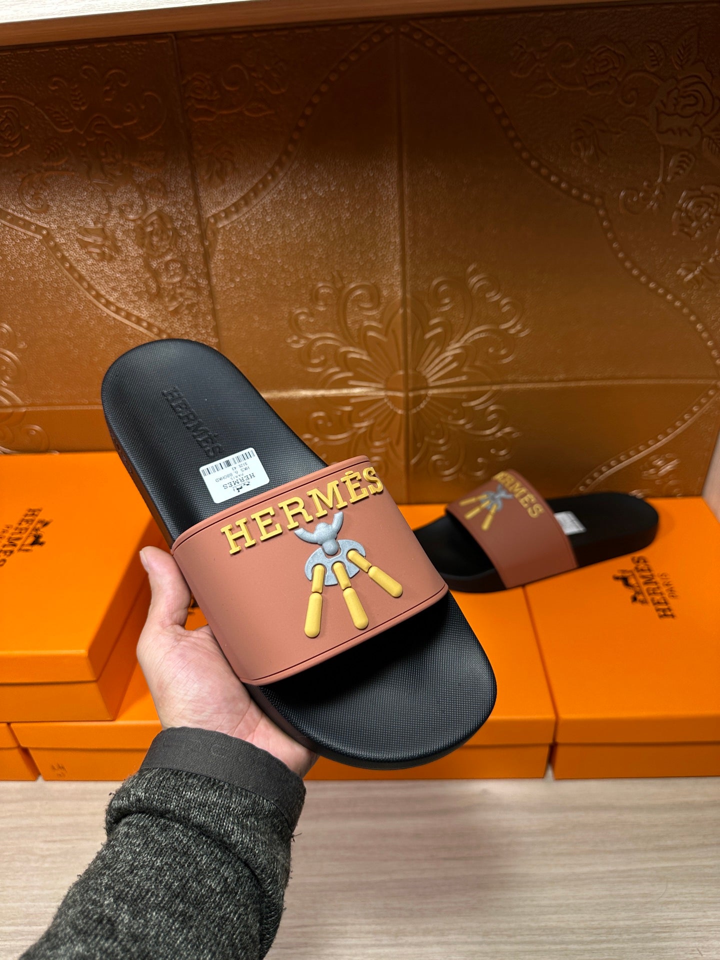 Hermes slide sandal held up: mauve strap on dark footbed with gold Hermes logo and motif.