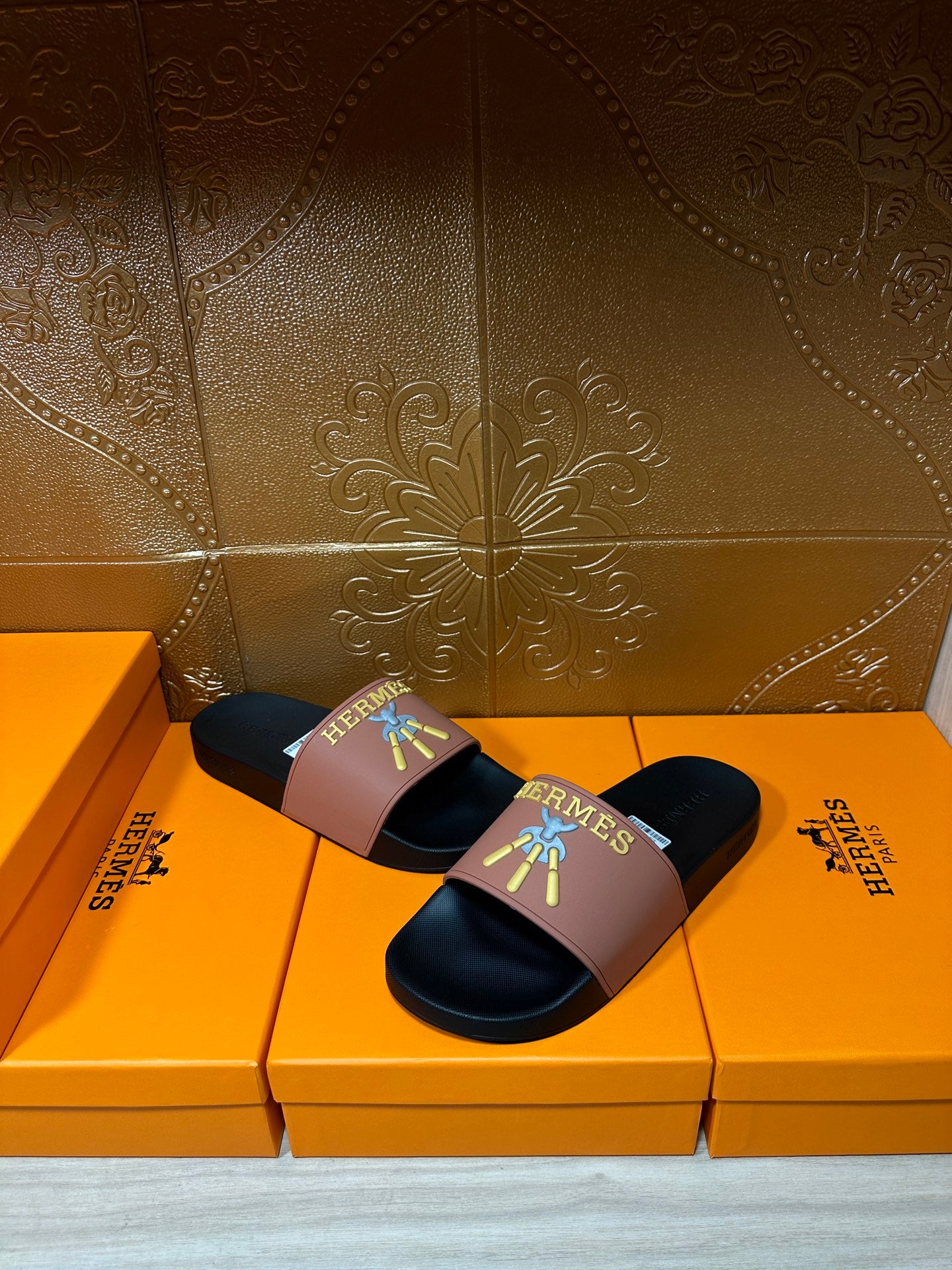 Hermes slide sandals with mauve strap and dark sole, gold Hermes logo and colorful detail.