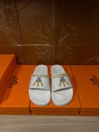 White Hermes slide sandals with single strap and gold logo on top