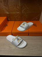 White Hermes slide sandals with gold logo, front and side pair view