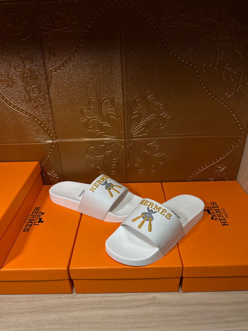 White Hermes slide sandals with gold emblem on strap, side view