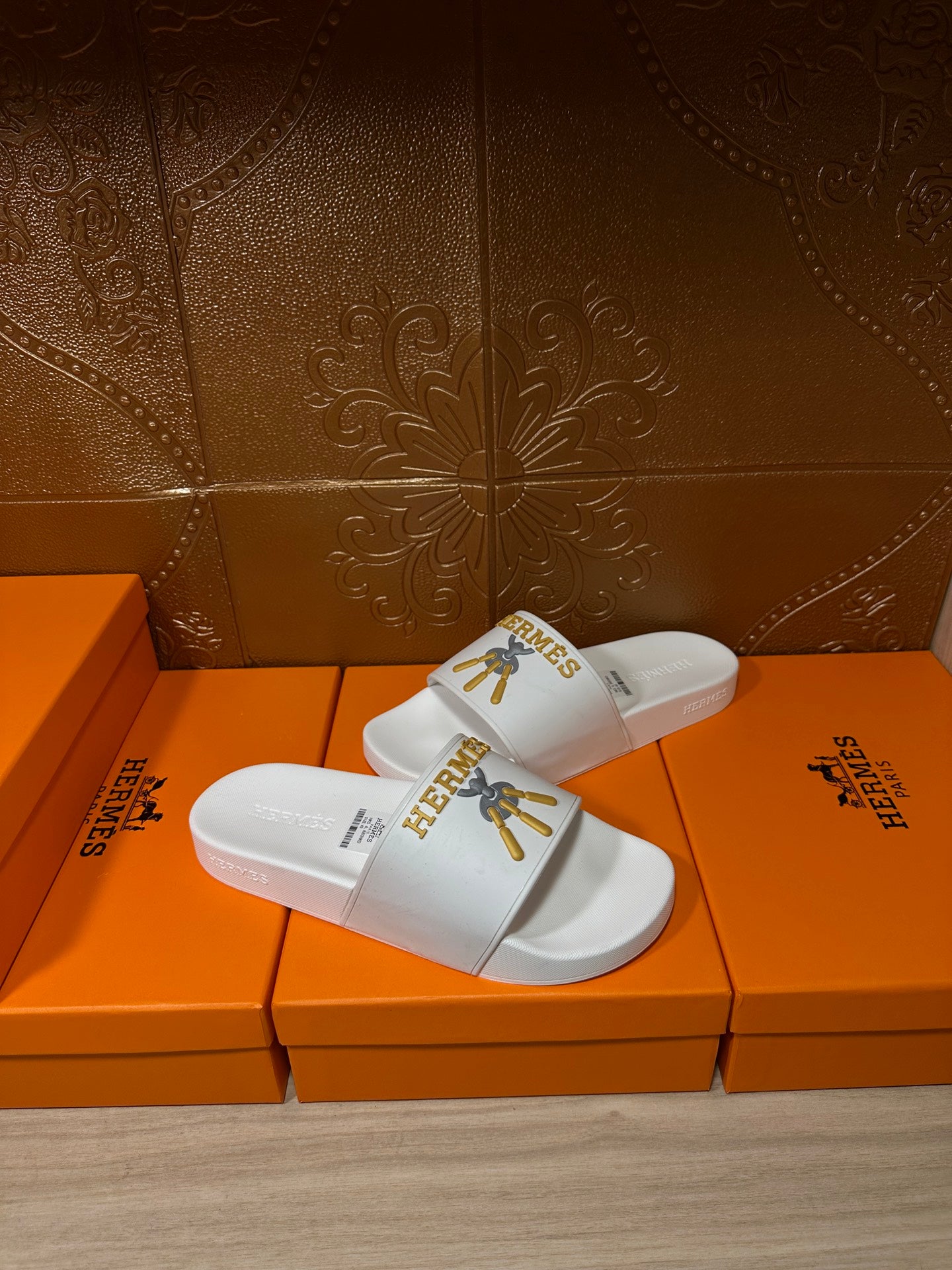White Hermes slide sandals with gold logo on front strap, angled view