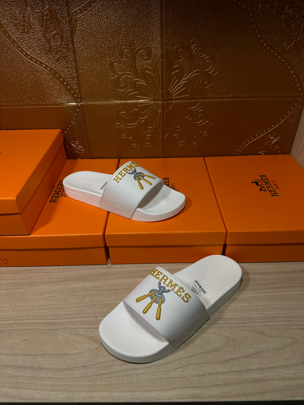 White Hermes slide sandals with gold emblem on top strap, two angles