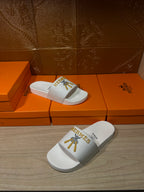 White Hermes slide sandals with gold emblem on top strap, two angles