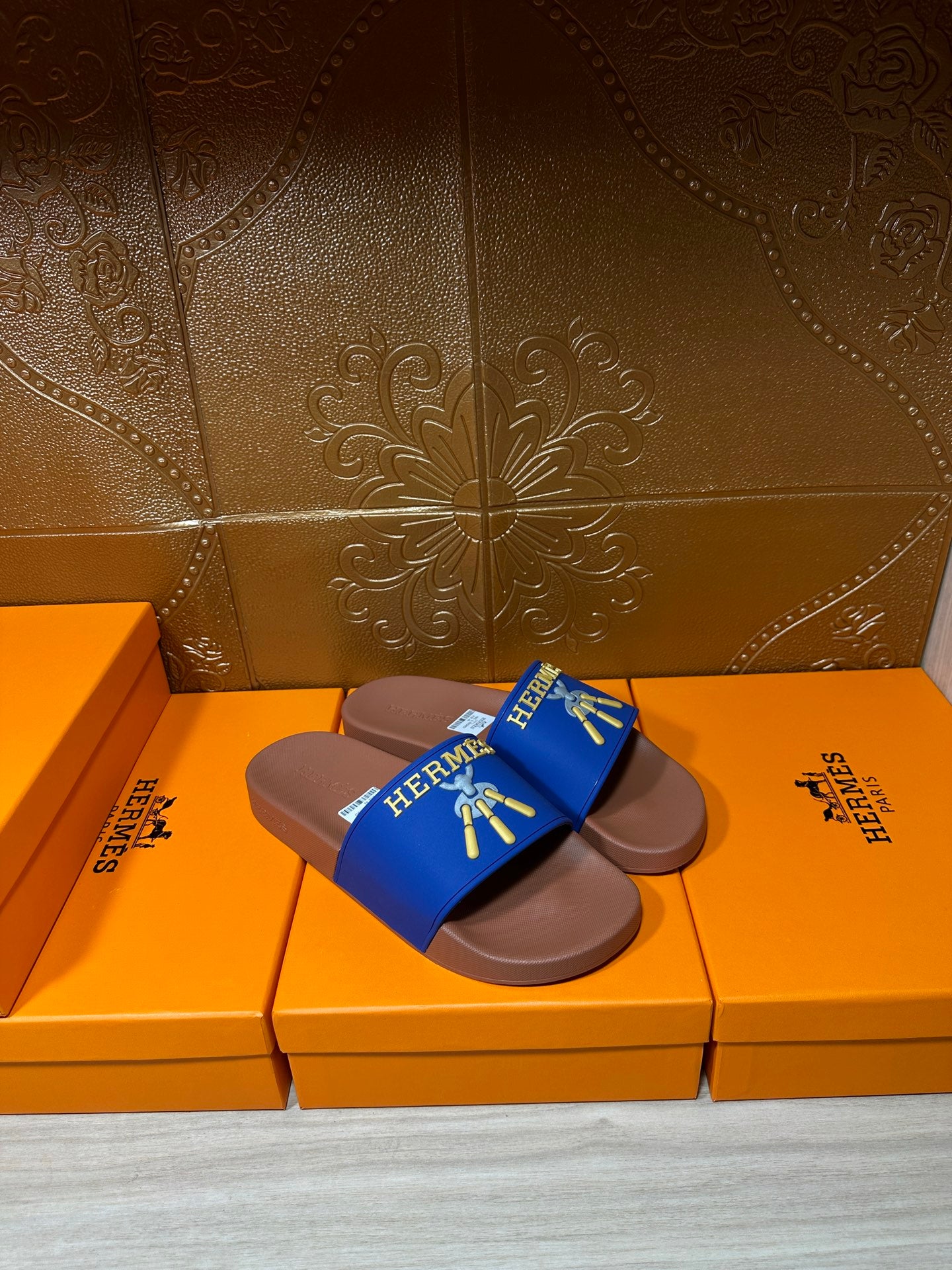 Hermès blue slide sandals with tan soles and gold logo graphic on strap