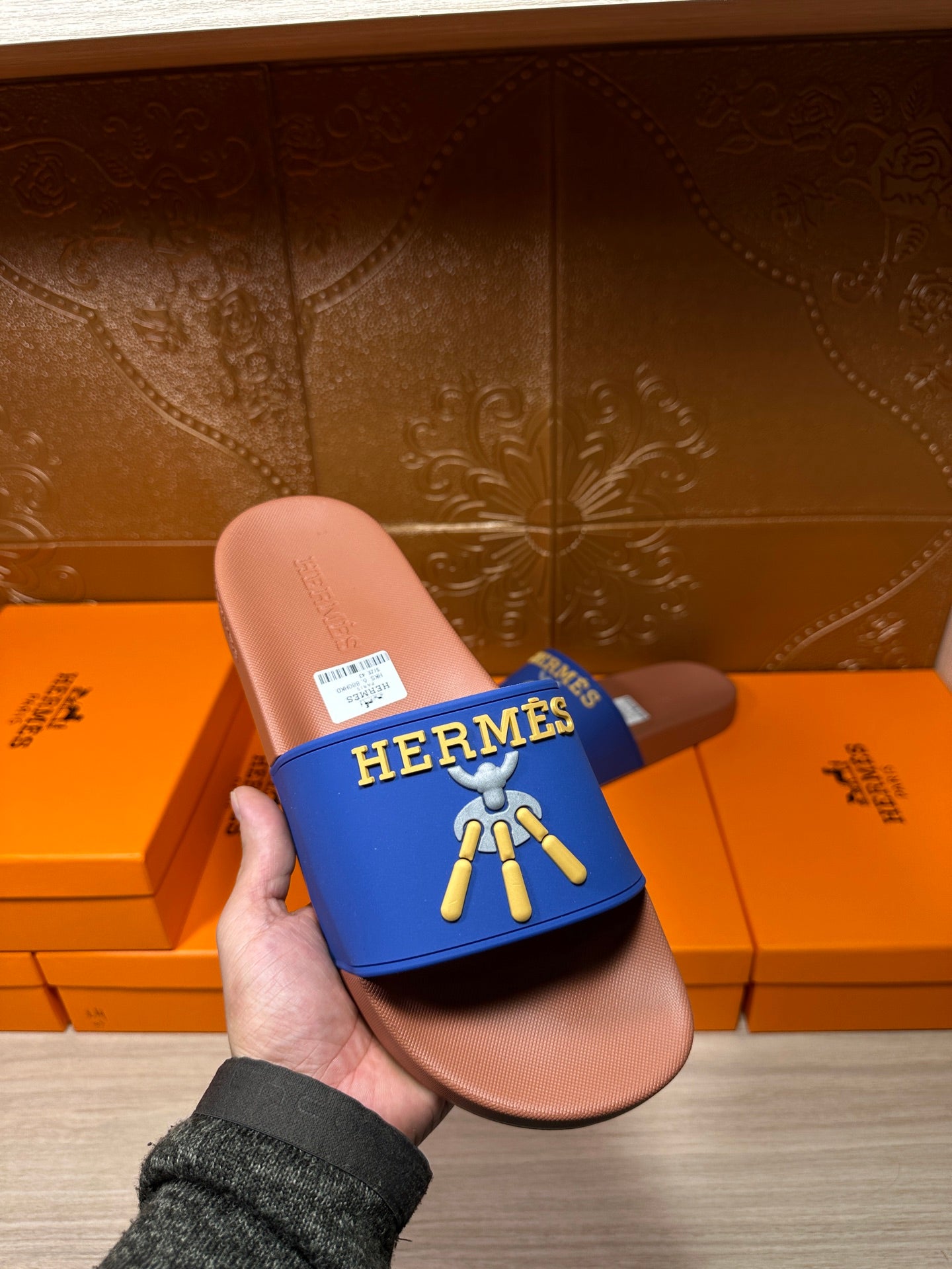 Hermès slide sandals held in hand, blue strap with gold logo, tan sole