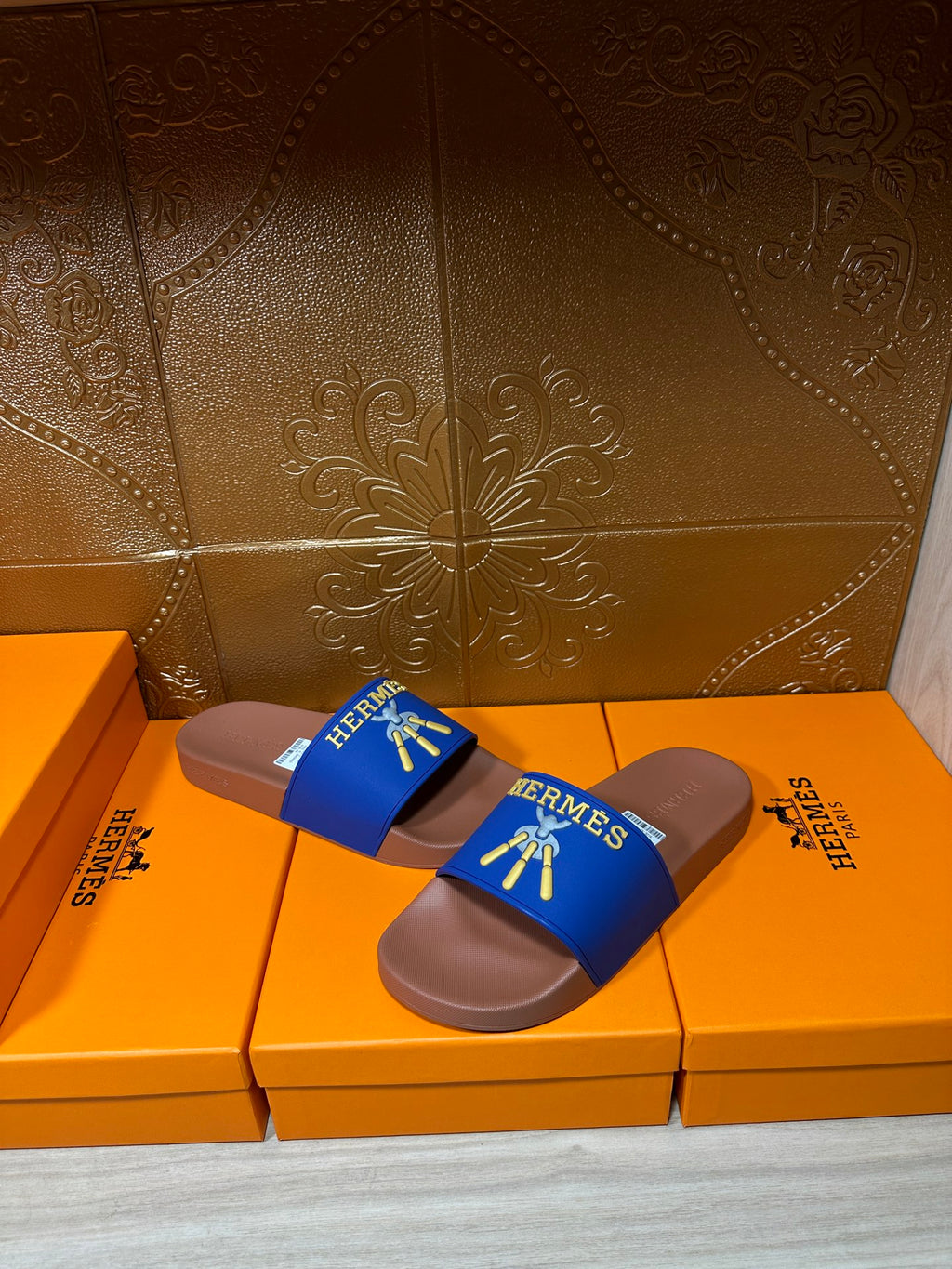 Hermès slide sandals with blue logo straps and tan soles, angled view