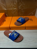 Hermès blue slide sandals with tan soles, laid flat with logo strap facing up