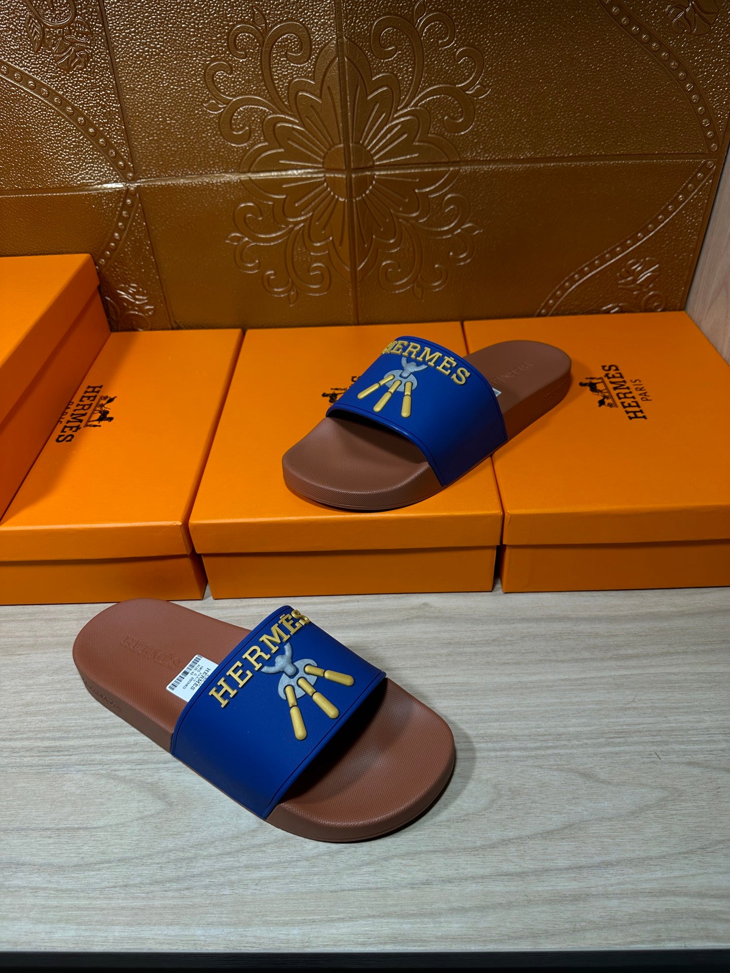 Hermès blue slide sandals with tan soles, laid flat with logo strap facing up