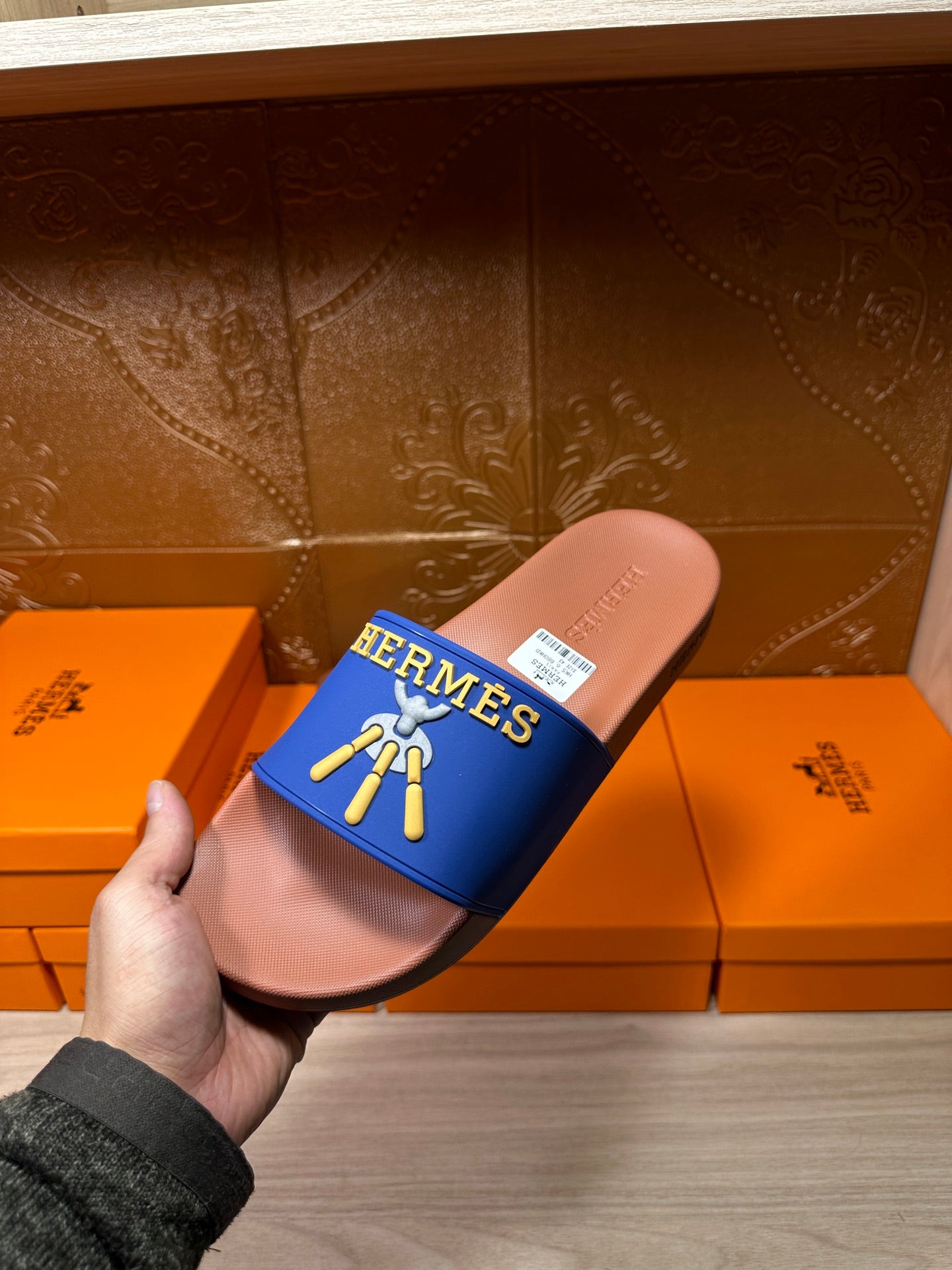 Hermès slide sandals held by hand, close-up of blue strap and tan footbed